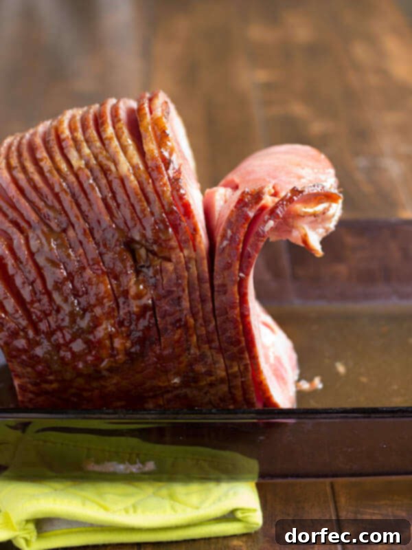 A perfectly cooked spiral ham, glistening with glaze, resting in a glass baking dish on a wooden surface, ready to be carved.