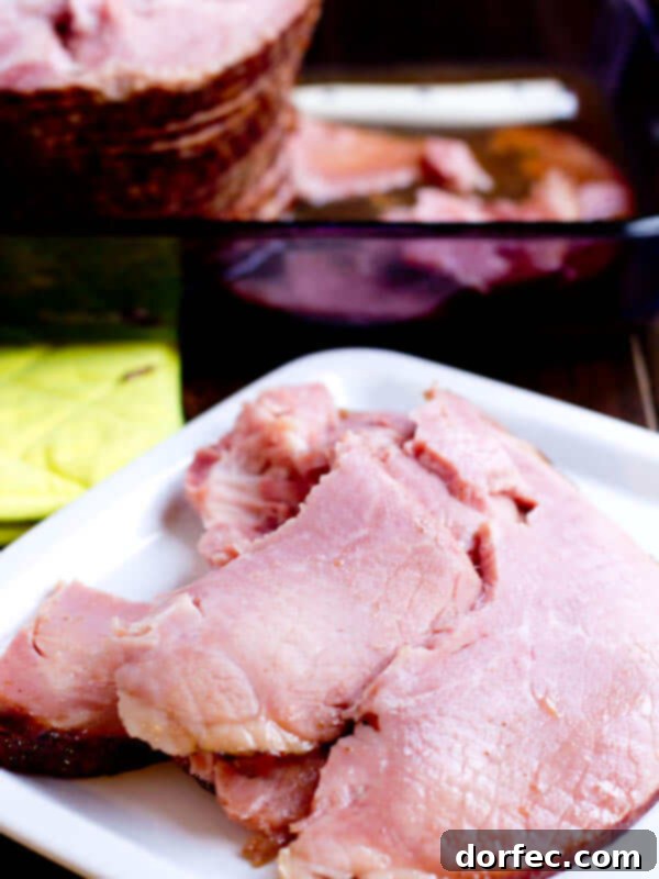 A serving of beautifully carved spiral ham slices arranged on a dinner plate, with a blurred whole spiral ham in the background.