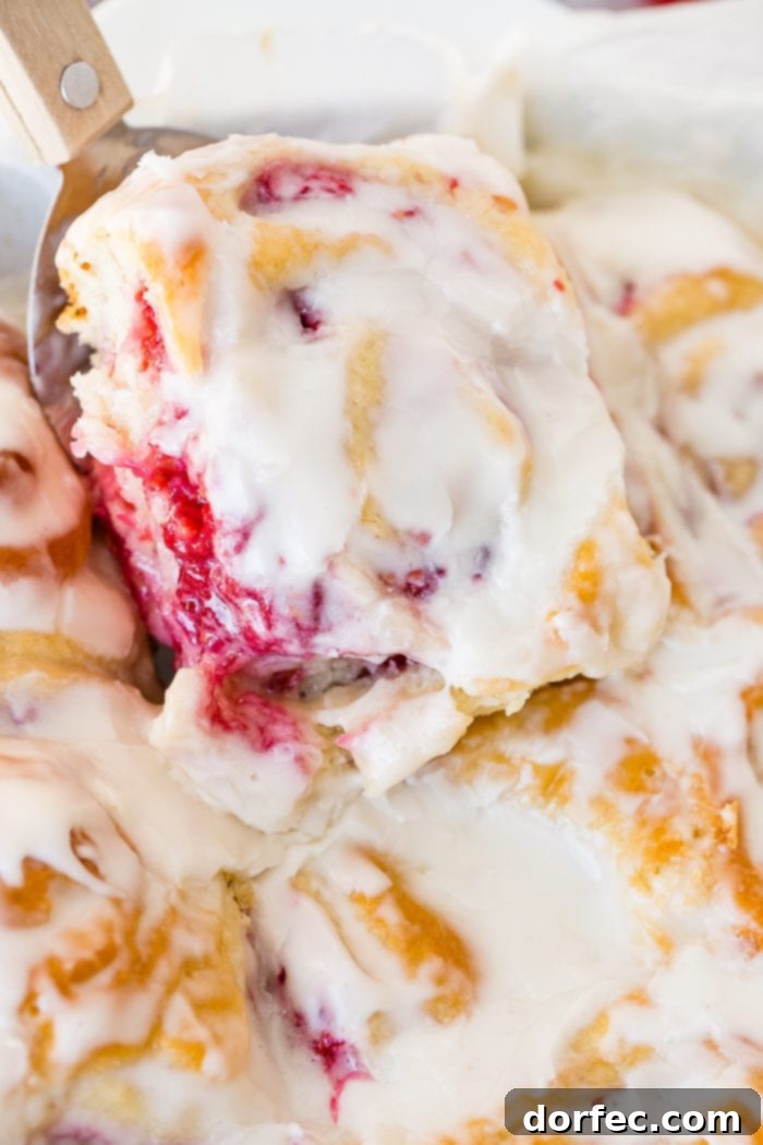 A frosted easy berry sweet bread being scooped out of a pan of baked sweet rolls with a spatula.