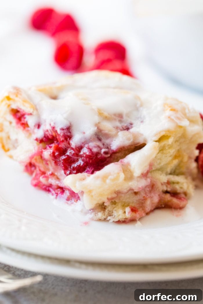 A photo of a easy berry sweet swirl roll sitting on a white plate and covered in frosting.