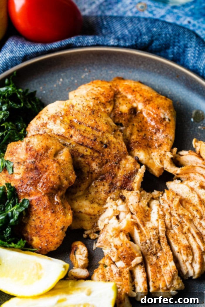 Effortless Traeger Smoked Chicken Breasts 2 A photo of whole smoked chicken breasts and sliced smoked chicken breasts on a charcoal gray plate with lemon wedges and kale on the side.
