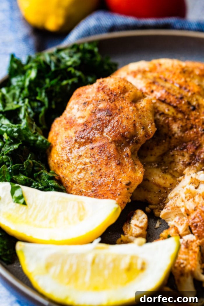 Effortless Traeger Smoked Chicken Breasts 3 A photo of whole smoked chicken breasts and on a charcoal gray plate with lemon wedges and kale on the side.