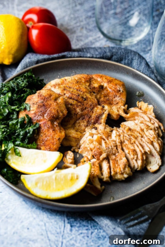 Effortless Traeger Smoked Chicken Breasts 4 A photo of whole smoked chicken breasts and sliced smoked chicken breasts on a charcoal gray plate with lemon wedges and kale on the side.