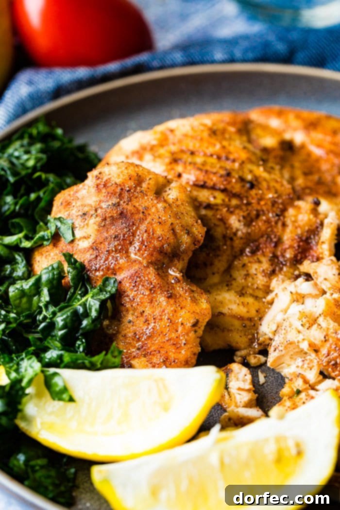 Effortless Traeger Smoked Chicken Breasts 6 A photo of whole smoked chicken breasts and sliced smoked chicken breasts on a charcoal gray plate with lemon wedges and kale on the side.