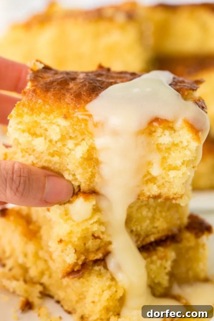 A person holding a fresh slice of homemade sweet cornbread, generously drizzled with honey butter.