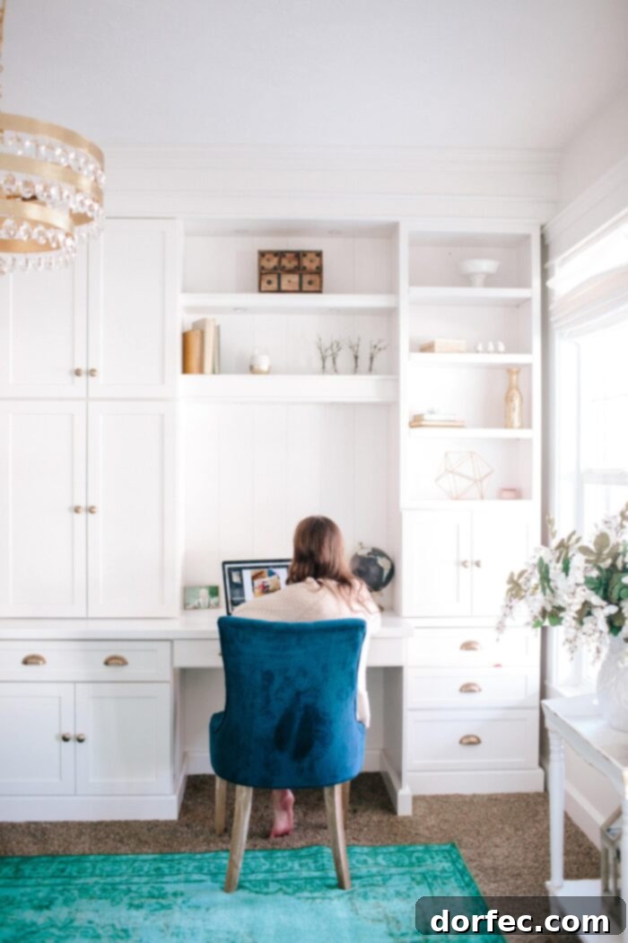 a white built in office with green upholstered chair and gold hardware with a gold chandelier