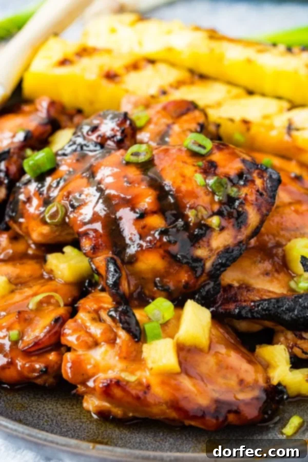 A photo of grilled huli huli chicken with grilled pineapple in the background.