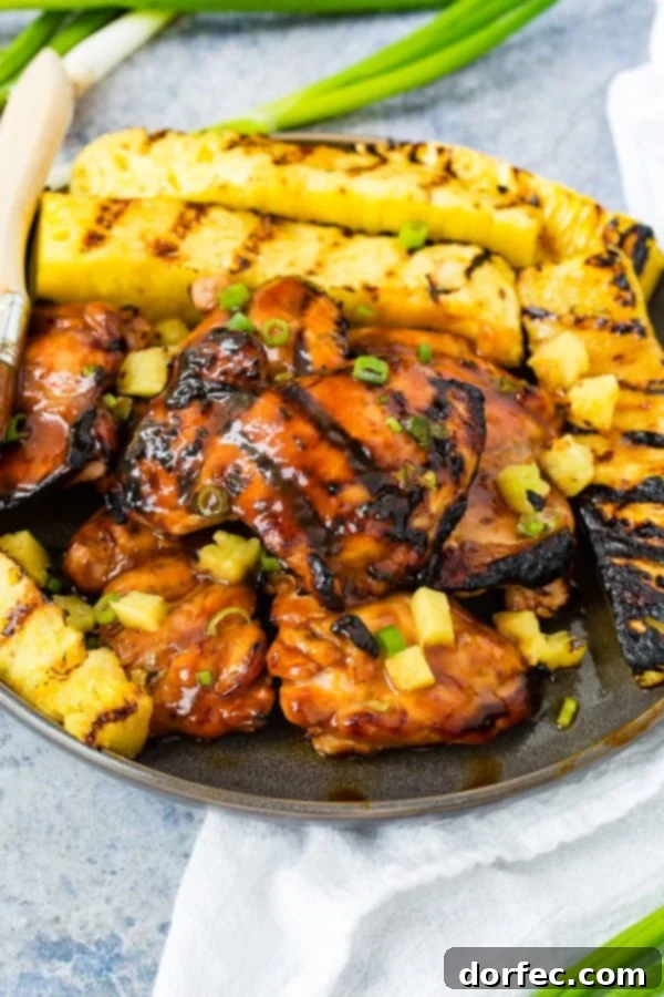 A photo of grilled huli huli chicken with grilled pineapple in the background.