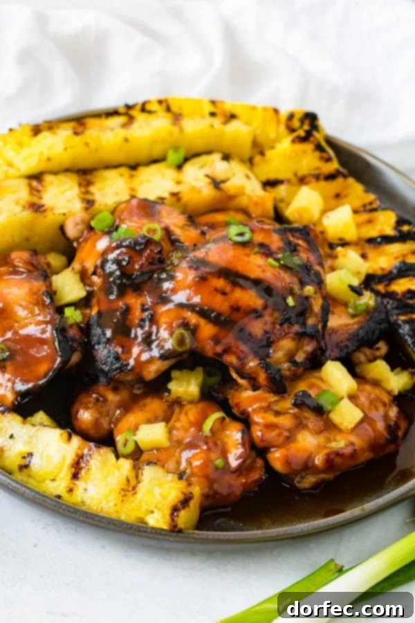 A photo of grilled huli huli chicken with grilled pineapple in the background.