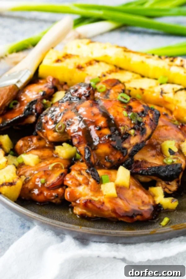 A photo of grilled huli huli chicken with grilled pineapple in the background.