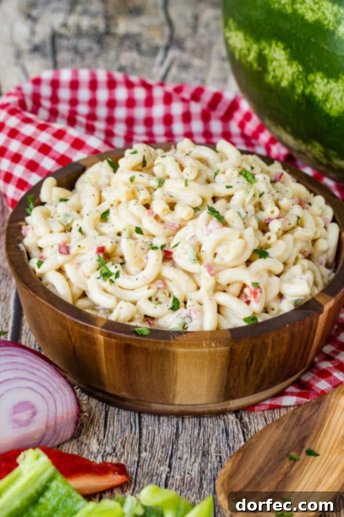 Ultimate Macaroni Pasta Salad Recipe 2 A wooden bowl on a red and white checkered napkin full of creamy cold noodles, ready to be served at a summer gathering.