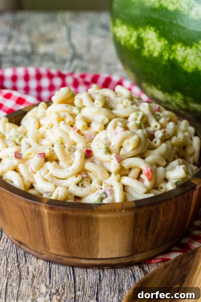 Ultimate Macaroni Pasta Salad Recipe 3 A wooden bowl on a red and white checkered napkin filled with creamy macaroni salad, ready for a summer party.