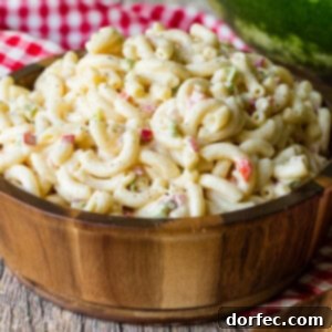 Ultimate Macaroni Pasta Salad Recipe 7 A wooden bowl on a red and white checkered napkin full of creamy macaroni salad.