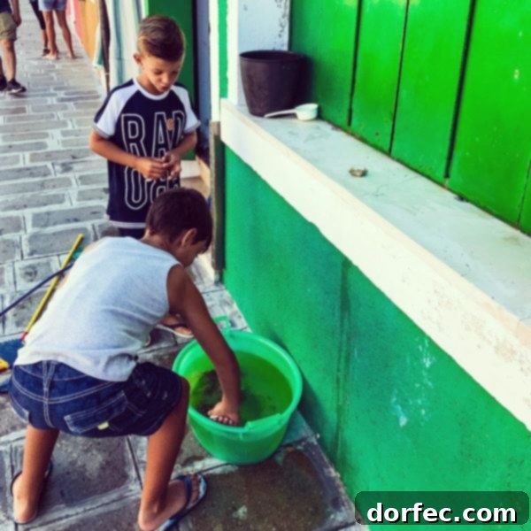 Two young boys playfully interacting with crabs in a bucket by a Venetian canal, a scene that evokes both innocence and the harsh realities of life.