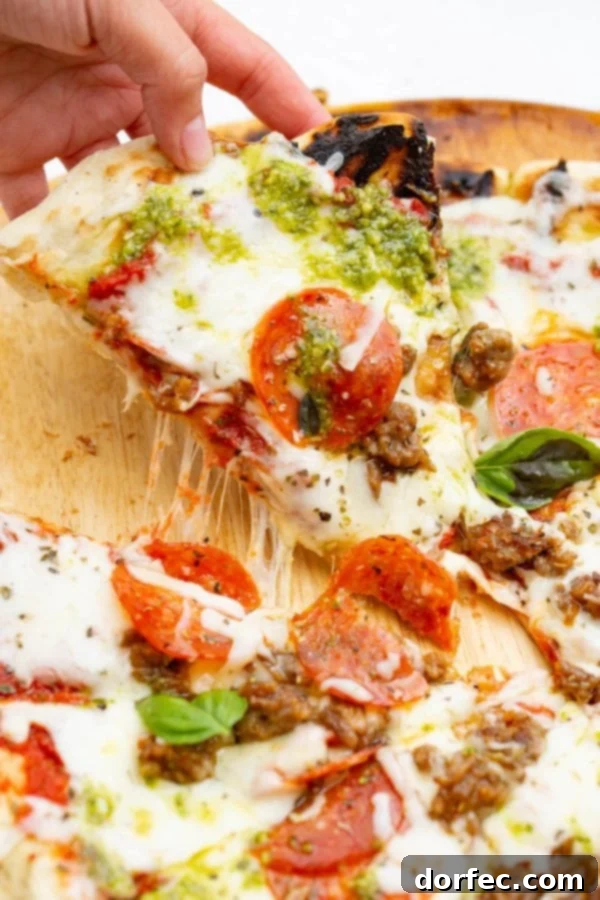 A photo of a piece of pesto pepperoni grilled pizza being pulled away from the whole pizza.