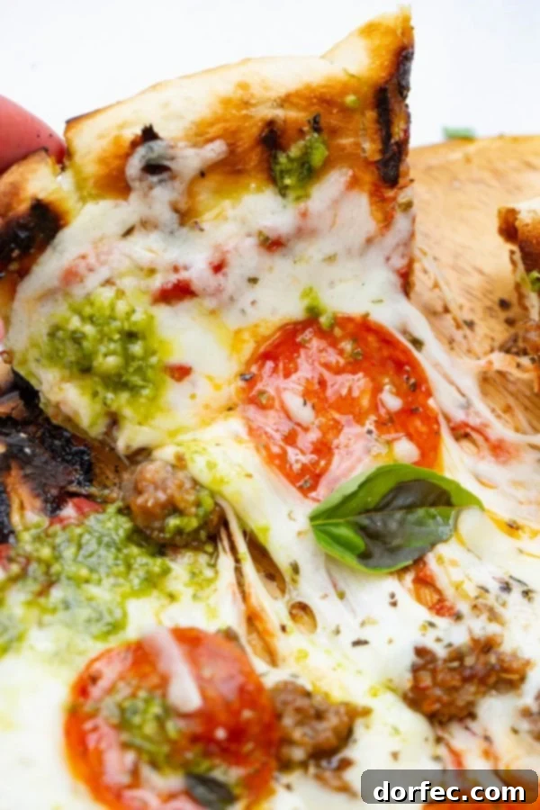 A photo of a piece of pesto pepperoni grilled pizza being pulled away from the whole pizza.