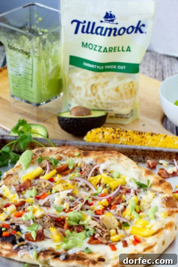Pulled Pork Pizza with Sweet Corn and Cilantro Cream A photo of pulled pork pizza covered in sweet corn, red onions, pinapple, bacon, and fresh cilantro with a cob of grilled corn in the background as well as a bag of Tillamook mozzarella cheese shreds.