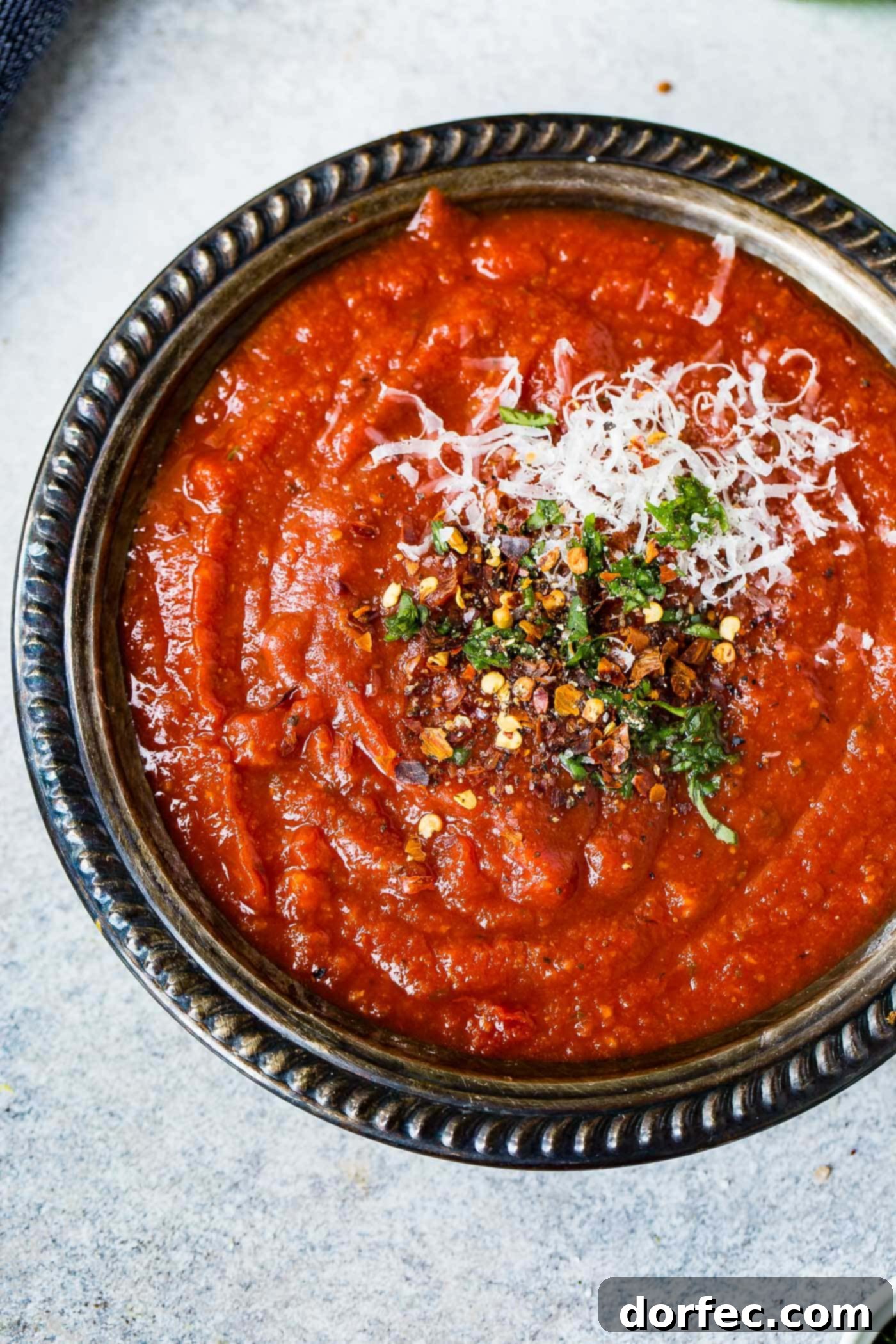 A black bowl of pizza sauce. The sauce is sprinkled with cheese and herbs.