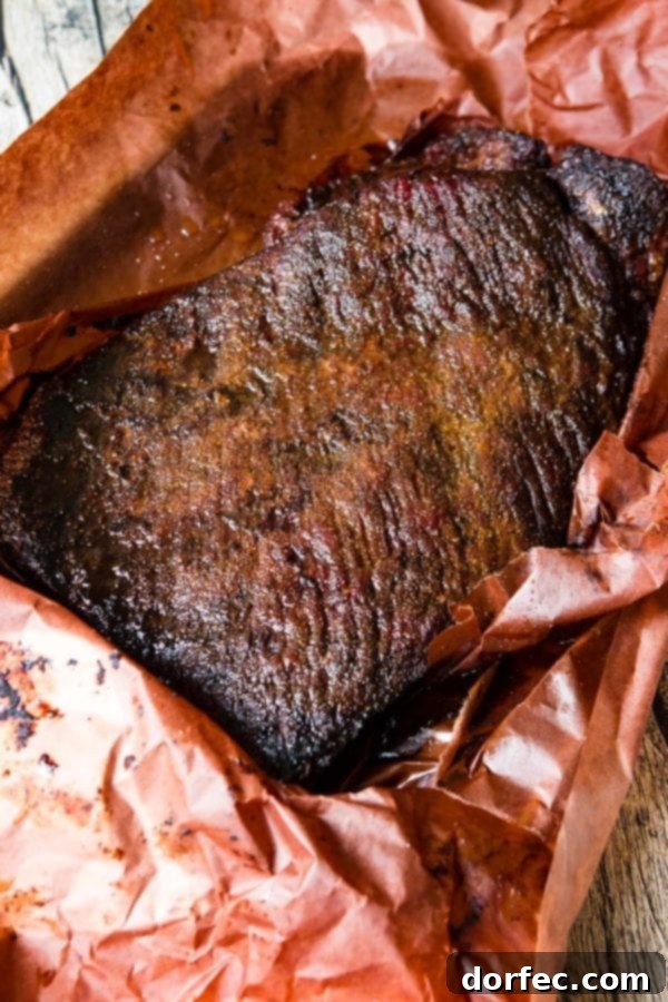 A photo of a perfectly smoked brisket with a delicious crusty bark sitting in peach butcher paper.