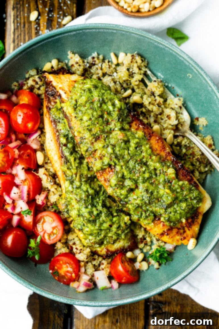 Light and Lean Pesto Tilapia Dinner 2 Two golden-brown tilapia fillets generously topped with bright green basil pesto, served on a bed of fluffy multi-colored quinoa, with a side of ripe grape tomatoes. The dish looks fresh, healthy, and inviting.