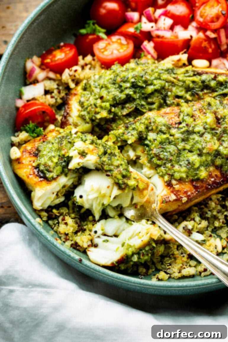 Light and Lean Pesto Tilapia Dinner 3 A fork gently flakes a piece of perfectly cooked tilapia, revealing its tender, white flesh, generously coated in bright green pesto sauce. This close-up highlights the dish's irresistible texture and flavor.