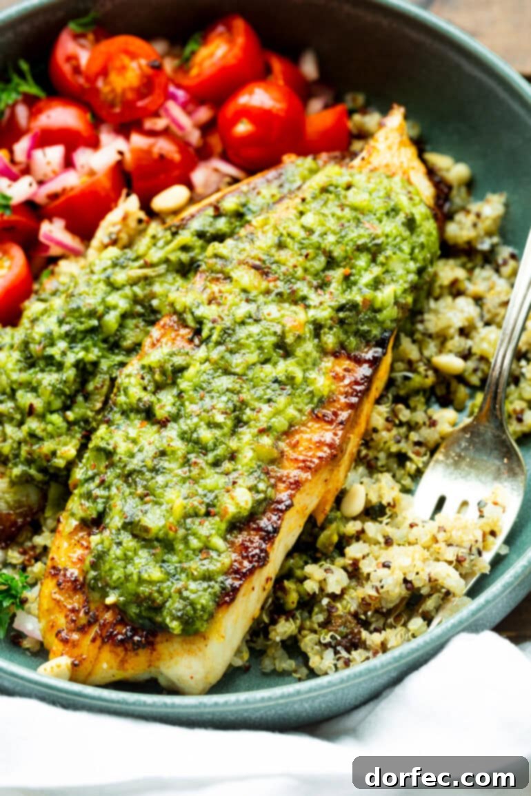 Light and Lean Pesto Tilapia Dinner 5 Two perfectly seared and golden-brown tilapia fillets, elegantly topped with vibrant basil pesto, presented on a colorful bed of multi-grain quinoa. The dish is inviting and highlights the natural beauty of the ingredients.