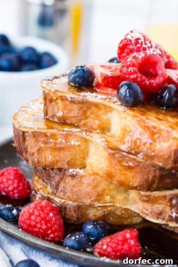 How to Make the Best French Toast A photo of a stack of 4 perfectly made french toast slices dripping with syrup and fresh berries, highlighting the best French toast recipe.