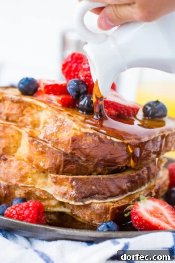 French Toast with Syrup and Berries A photo of syrup being poured generously over a stack of golden-brown French toast covered in fresh berries.