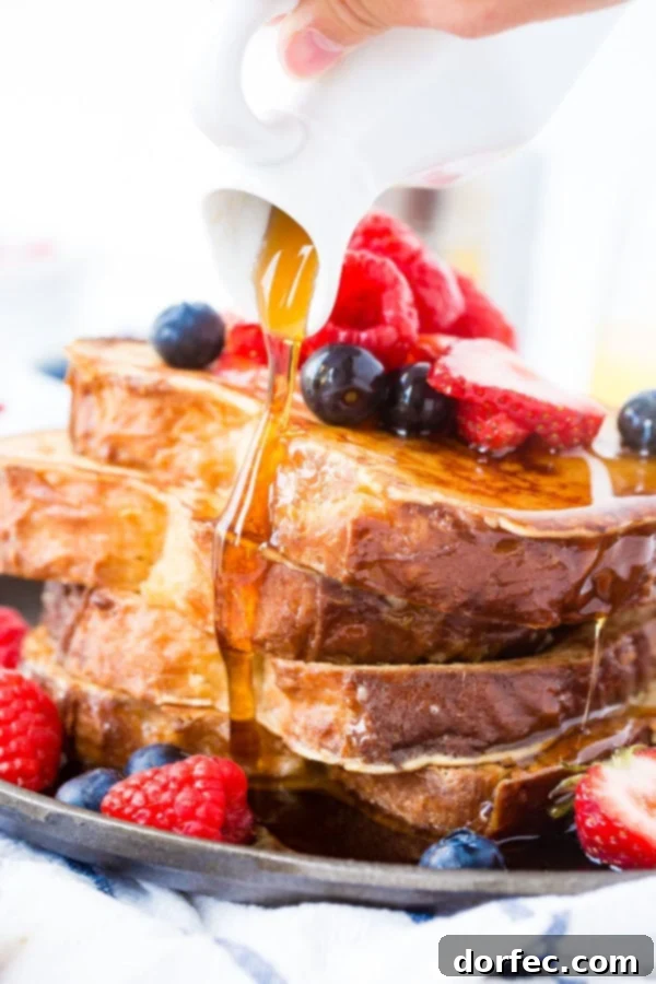 French Toast Toppings Inspiration A photo of rich syrup being poured over a stack of golden French toast adorned with fresh berries, showcasing enticing toppings.