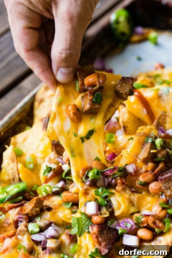 A hand reaching for a single cheesy nacho chip, pulling it from a delectable pile of BBQ brisket nachos, showcasing the irresistible gooey cheese.