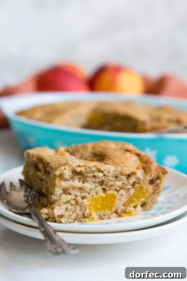 A golden-brown slice of homemade peach dump cake on a white plate, garnished with a sprinkle of powdered sugar and a hint of a fork.