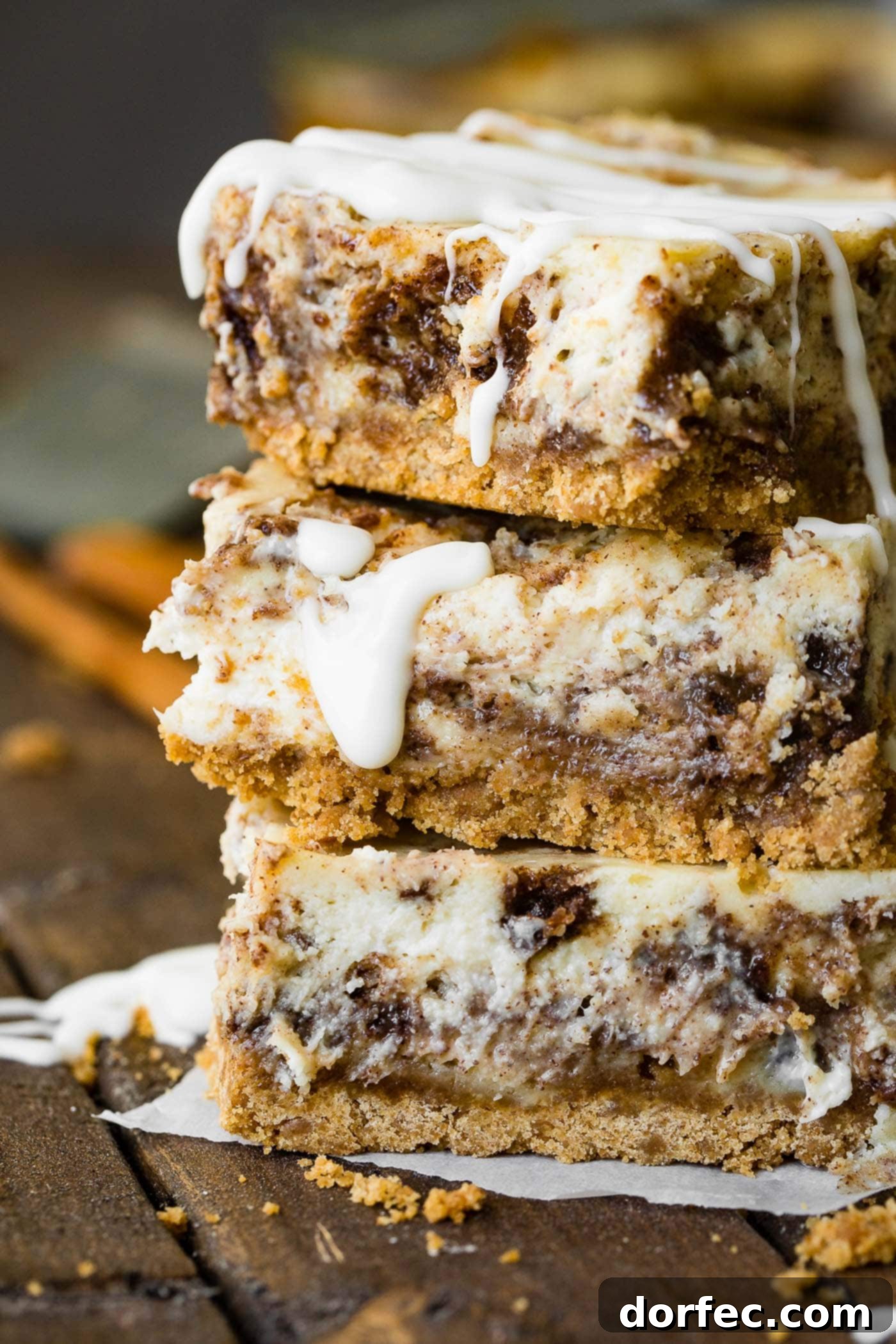 A photo of three cinnamon roll cheesecake bars stacked on top of each other, showcasing the cinnamon swirl and golden crust.
