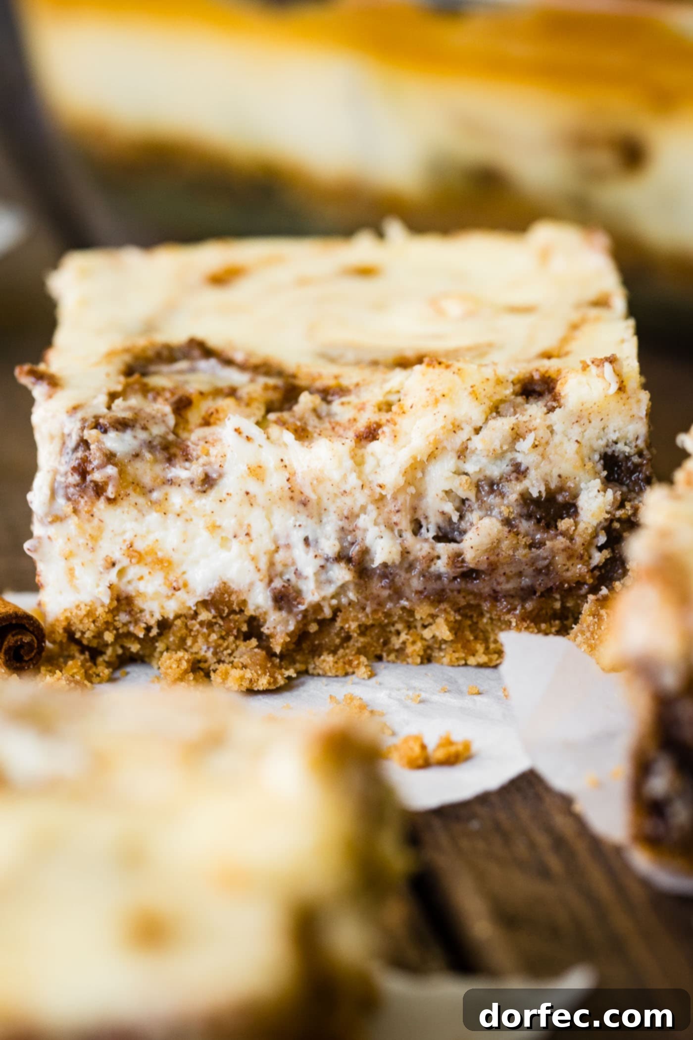 A close-up photo of a single cinnamon roll cheesecake bar, showing the layers of crust, cheesecake, and cinnamon swirl.