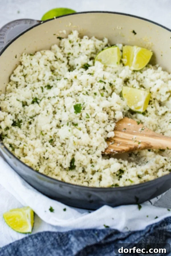 A photo of a pot full of Cilantro Lime Cauliflower Rice with fresh lime wedges on top and a wooden spoon, emphasizing its fresh ingredients.