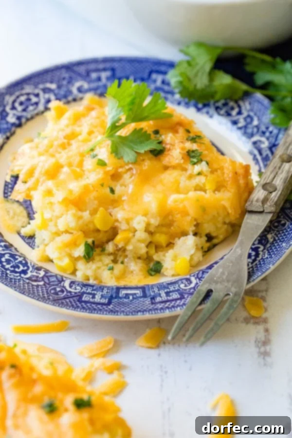 A vibrant serving of cheesy Jiffy corn casserole on a blue and white plate, with a fork resting beside it, highlighting its golden-brown crust and creamy texture.