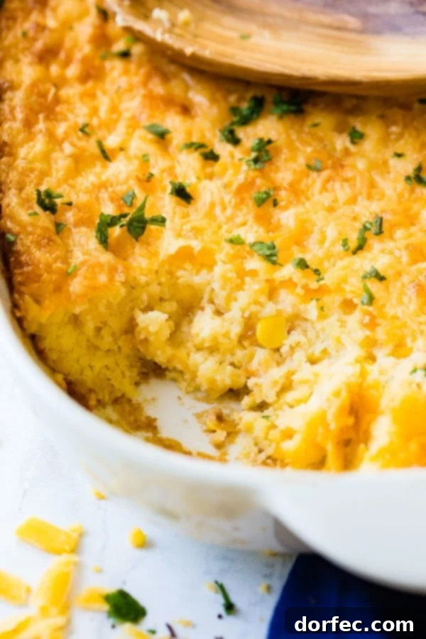 A baking dish filled with golden-brown Jiffy corn casserole, with a large serving removed, revealing its creamy interior.