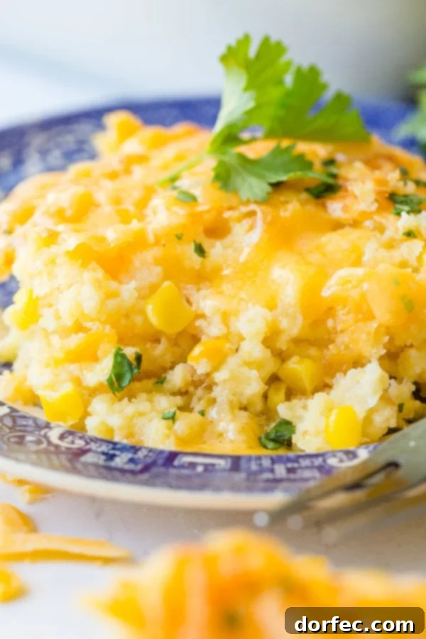 A serving of golden-brown cheesy Jiffy corn casserole on a blue and white plate, with a silver fork ready for digging in.