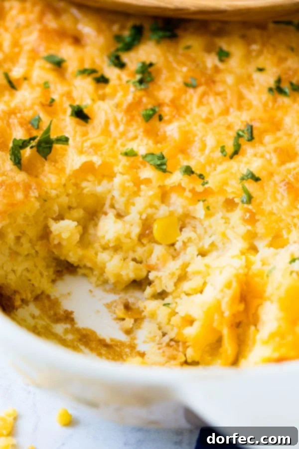 A large baking dish filled with golden-brown Jiffy corn casserole, with one serving elegantly scooped out, showcasing its rich, creamy texture.