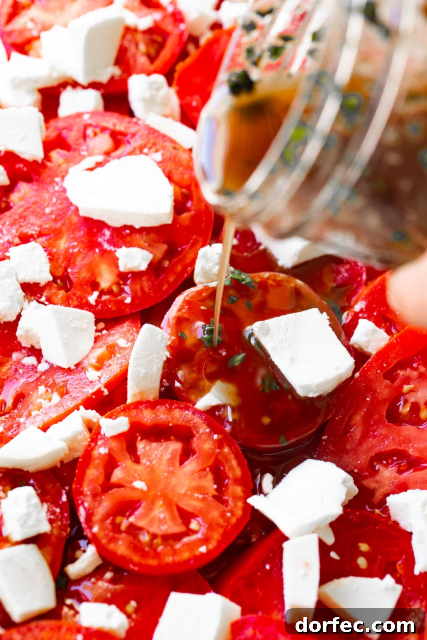 A photo of balsamic vinegar dressing being poured over marinated tomatoes salad.