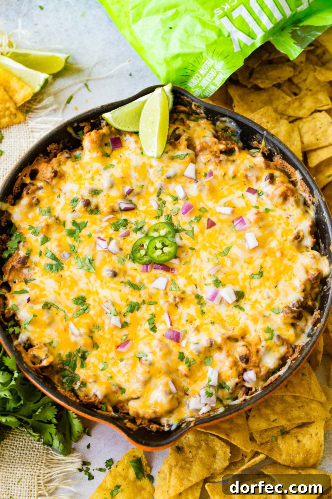 Easy One Skillet Cheesy Black Bean Dip A photo of a cast iron skillet full of black bean dip covered in melted cheese and topped with diced red onion, fresh cilantro, sliced jalapenos and lime wedges.