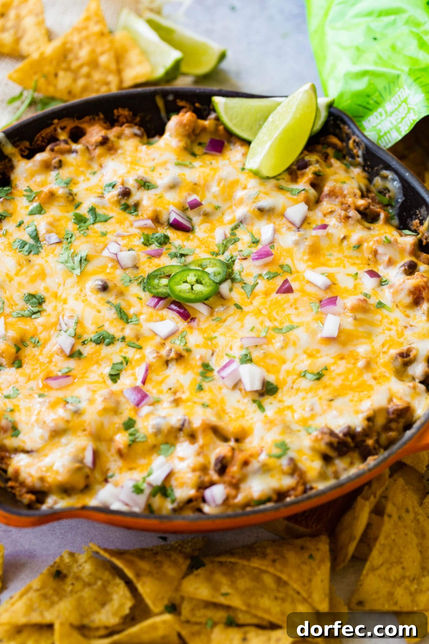 Easy One Skillet Cheesy Black Bean Dip A photo of a cast iron skillet full of black bean dip covered in melted cheese and topped with diced red onion, fresh cilantro, sliced jalapenos and lime wedges.