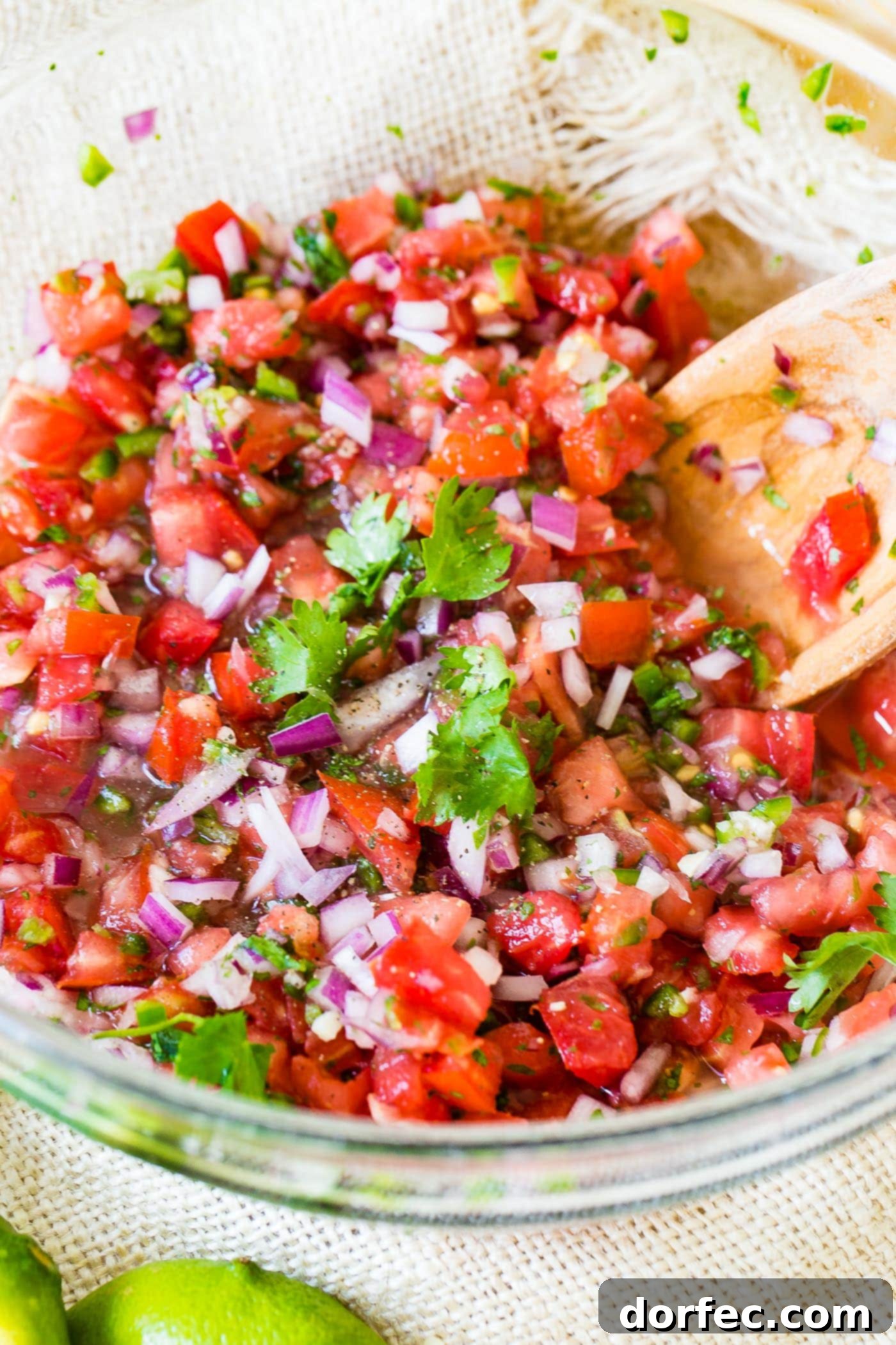 A wooden spoon gently stirring a vibrant bowl of homemade Pico de Gallo, showcasing the perfect chunky texture and rich colors of the fresh ingredients.