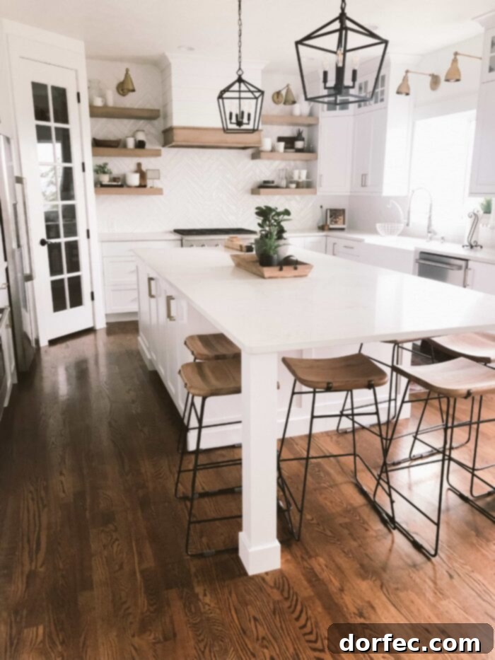 Stunning all-white kitchen with a spacious island, elegant white countertops, glass-front cabinets, and black pendant lights, featuring natural wood floating shelves and a full pantry door with glass inserts
