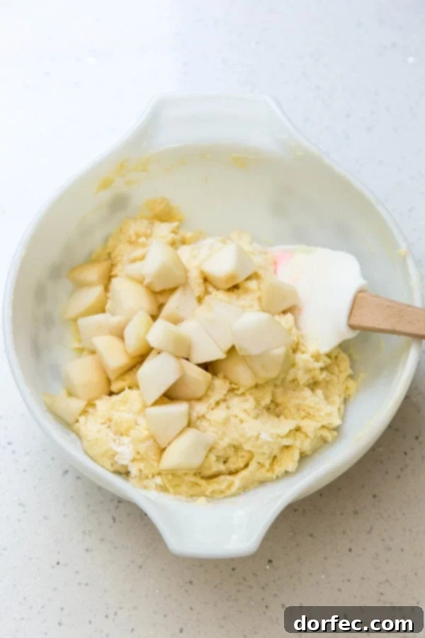 Folding diced pears into cake batter, highlighting the texture and fruit distribution