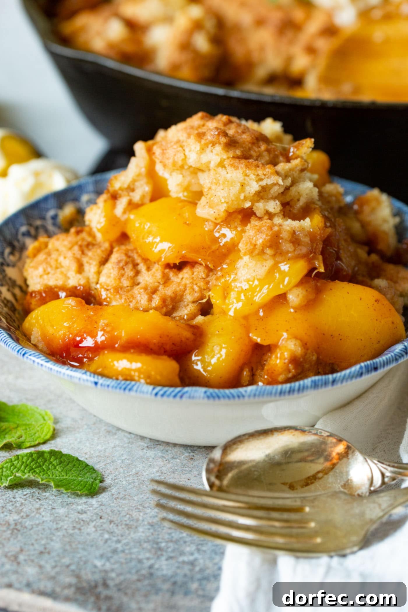 A photo of a bowl of peach cobbler with a biscuit topping, steam gently rising from the warm dessert.