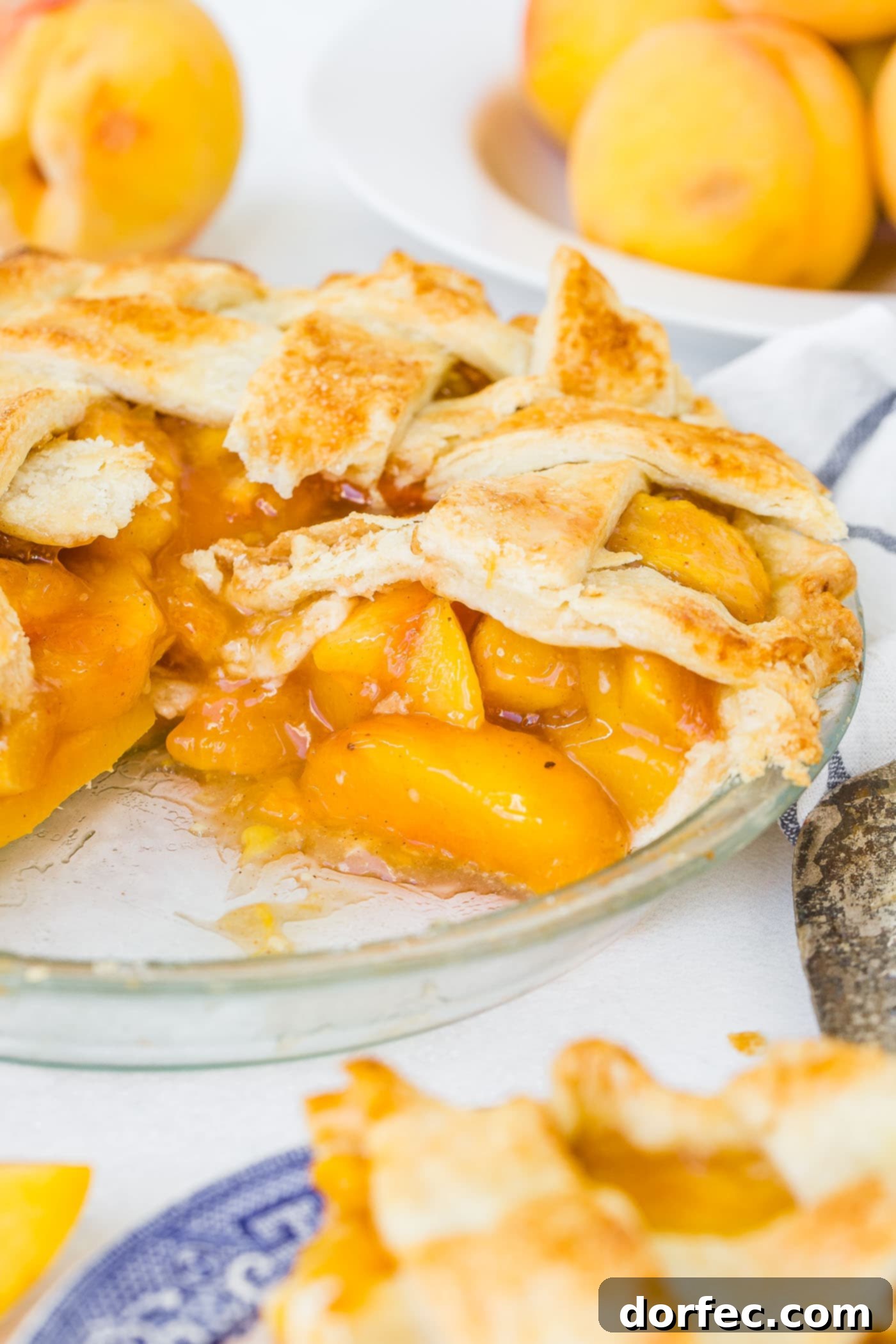 A photo of a fresh peach pie with a couple of slices missing and one slice ready to serve.