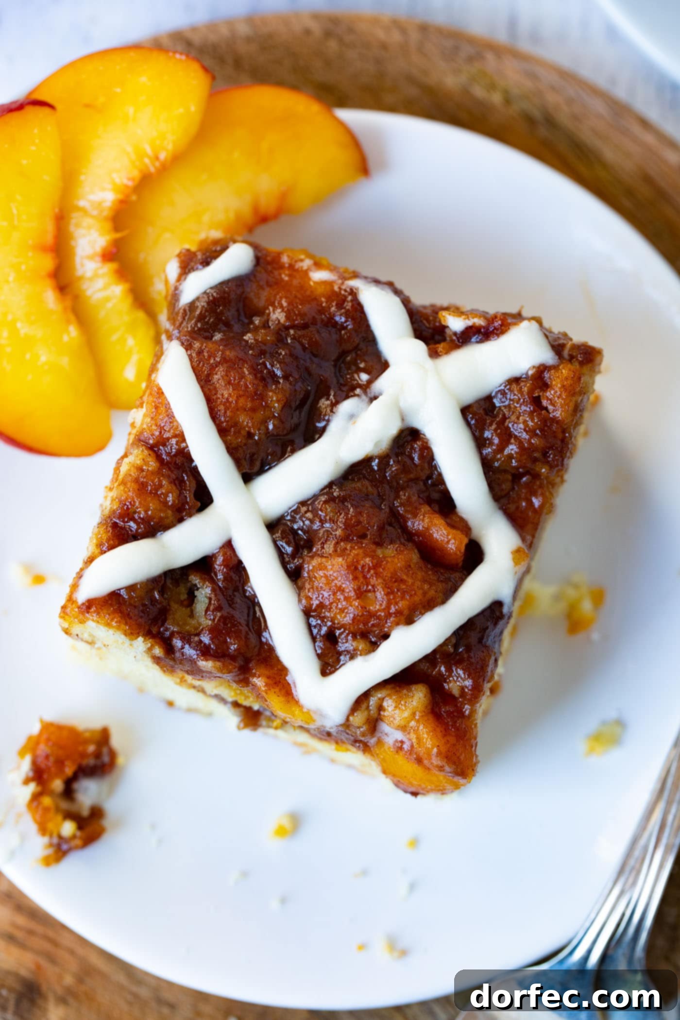 A single piece of easy peach sour cream coffee cake, beautifully glazed, is presented on a white plate with three fresh peach slices beside it.