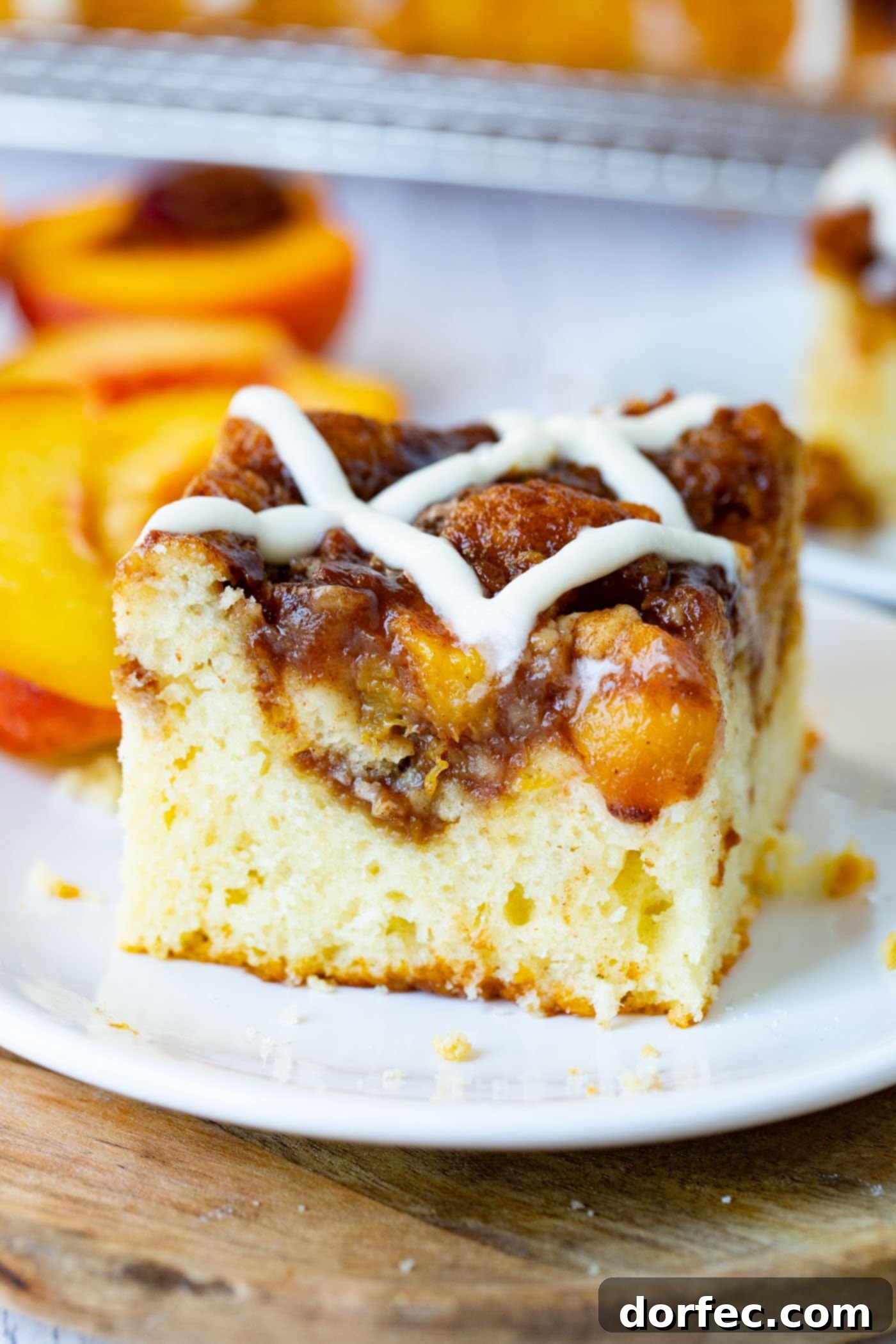 A close-up photo of a single piece of easy peach sour cream coffee cake, topped with a glistening sweet glaze, resting on a pristine white plate.