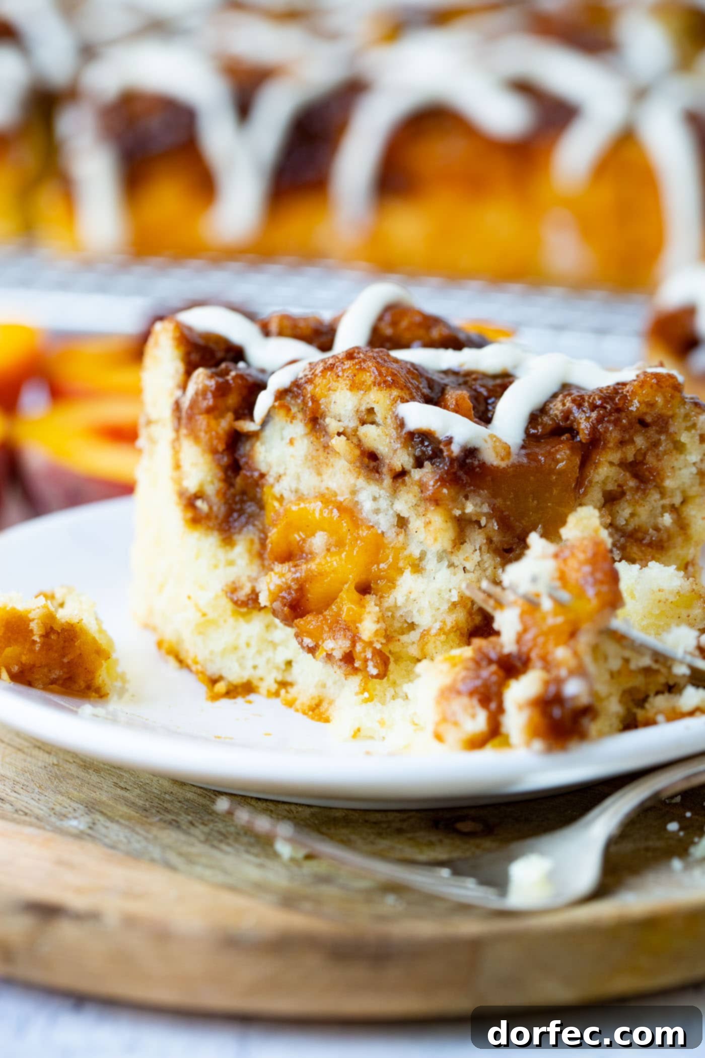 A single piece of peach coffee cake, with a fork cutting into it, reveals the moist crumb and juicy peach filling.