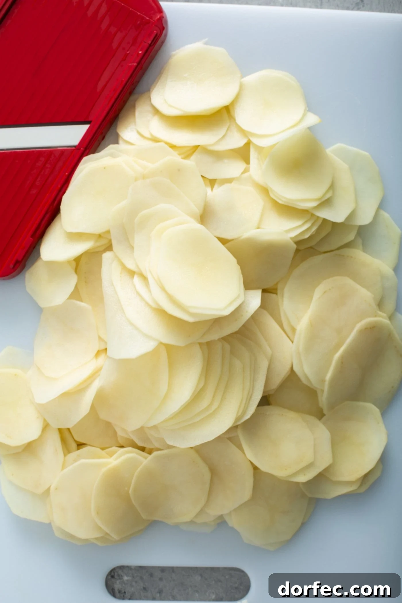 Raw, peeled, sliced potatoes with a red and white kitchen towel in the background.